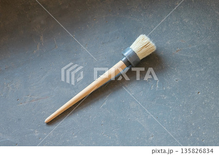 hand held paint brush designed for priming and painting surfaces. Round paint brush with wooden handle for priming and painting work on gray textured surface. Tool for home renovation and maintenance 135826834