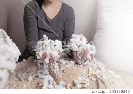 Woman fills a pillow case with foam rubber. Foam pieces, crumbs. Woman repairs furniture pillows. White polyurethane foam rubber pieces. stuffing for pillows and furniture. photo Woman fills a pillow case with foam rubber. Foam pieces, crumbs. Woman repairs furniture pillows. White polyurethane foam rubber pieces. stuffing for pillows and furniture. photo 135826846