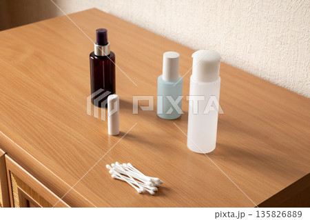 Cosmetic bottles and cotton swab on wooden table for beauty product advertisement. Minimalist essential personal care items. Cosmetic bottles and cotton swab on wooden table for beauty product advertisement. Minimalist essential personal care items. 135826889