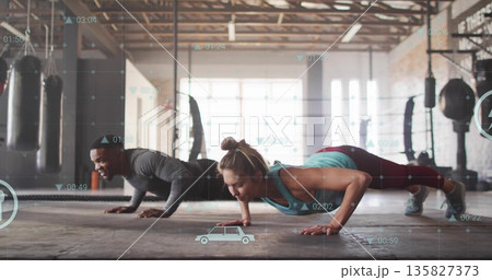 Holding push-ups training partners wearing athletic wear in warehouse gym, with digital overlays 135827373
