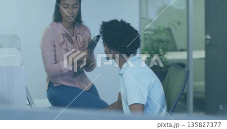 Holding black tablet, woman wearing pink blouse, speaking to coworker in office with silver laptop Holding black tablet, woman wearing pink blouse, speaking to coworker in office with silver laptop 135827377