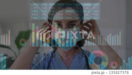 Adjusting surgical mask, female healthcare worker reviewing charts in clinic room, with stethoscope Adjusting surgical mask, female healthcare worker reviewing charts in clinic room, with stethoscope 135827378