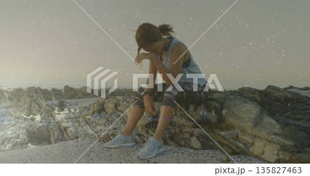 Resting athletic woman leaning forward on pebbled coastal shore, with fitness watch, running shoes Resting athletic woman leaning forward on pebbled coastal shore, with fitness watch, running shoes 135827463