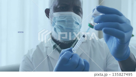 Drawing liquid from vial into syringe healthcare worker in lab coat, mask and gloves in clinic Drawing liquid from vial into syringe healthcare worker in lab coat, mask and gloves in clinic 135827495