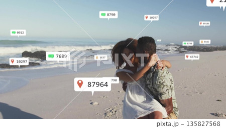 Carrying man in patterned shirt cradling woman in white dress on sandy shoreline with digital icons 135827568