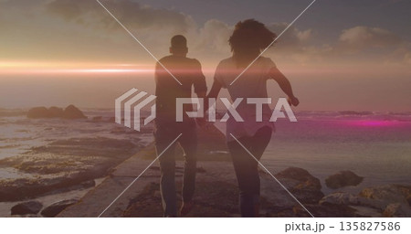 Walking couple holding hands on concrete pier at seaside sunset, with tidal pools and rock outcrops 135827586