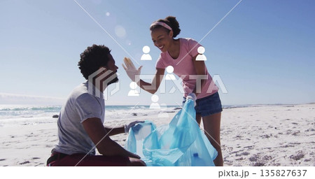 Collecting litter gloved shore cleanup volunteers working on sandy beach, holding blue bag 135827637