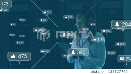 Monitoring server racks, IT pro with headset holding tablet in data center, with notifications 135827763