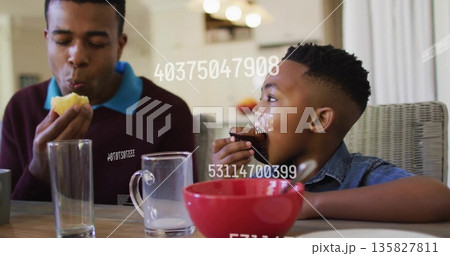Eating father and son biting muffin and chocolate cupcake at wooden table, with overlaid numbers Eating father and son biting muffin and chocolate cupcake at wooden table, with overlaid numbers 135827811