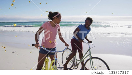 Walking two friends pushing pastel bicycles on sandy beach, smiling amid gold star-shaped elements Walking two friends pushing pastel bicycles on sandy beach, smiling amid gold star-shaped elements 135827817