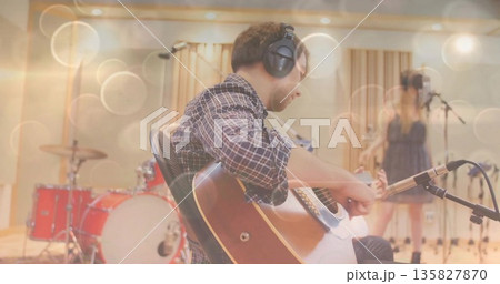 Male guitarist wearing plaid shirt, playing acoustic guitar in recording studio, with red drum kit Male guitarist wearing plaid shirt, playing acoustic guitar in recording studio, with red drum kit 135827870