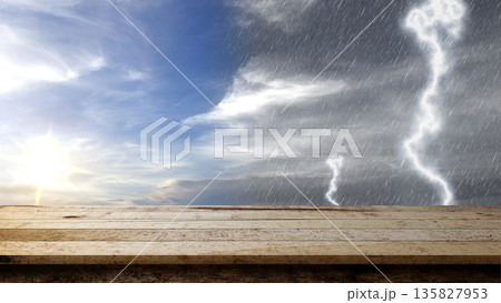Empty rustic wooden table with a background of contrasting weather, showing a bright sunny sky on one side and a dark stormy sky with rain and lightning on the other 135827953