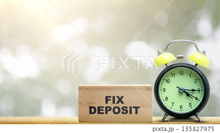 A wooden block with FIX DEPOSIT text next to an alarm clock on a wooden table, symbolizing time-bound financial investments and savings planning with copy space 135827975