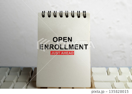A spiral notebook with 'Open Enrollment Just Ahead' message placed on a white computer keyboard. Concept for health insurance, employee benefits period, and work administration 135828015