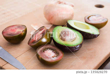 vegetables black tomatoes, avocado and onions on wooden board 135828270