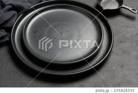 Two empty black matte plates lie on a dark textured table Two empty black matte plates lie on a dark textured table 135828335