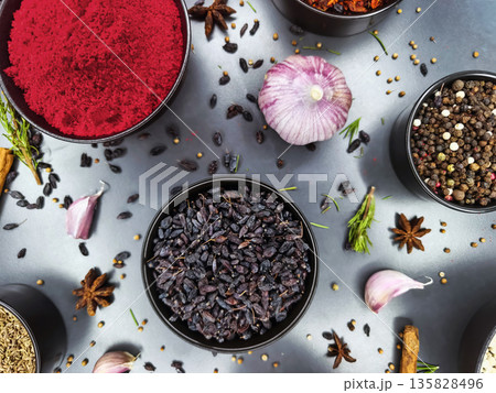 Colorful spices and herbs arranged in bowls on a kitchen counter with garlic and seeds nearby during daytime 135828496