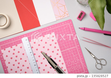 Pink sheet with ruler and knife on cutting mat among craft tools and colored paper. Creative workspace for art and design preparation. Pink sheet with ruler and knife on cutting mat among craft tools and colored paper. Creative workspace for art and design preparation. 135828527