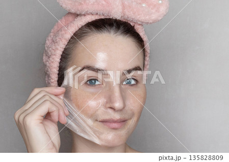 Caucasian woman makes a cosmetic Peel Off Mask. She removes the film mask with her hand Close up, copy space photo Caucasian woman makes a cosmetic Peel Off Mask. She removes the film mask with her hand Close up, copy space photo 135828809