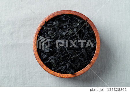 Top view of dried wakame seaweed in a wooden bowl on a fabric background Top view of dried wakame seaweed in a wooden bowl on a fabric background 135828861