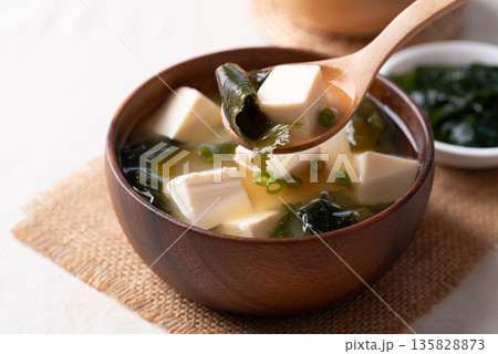 Healthy Japanese miso soup with soft tofu and seaweed in a wooden bowl being scooped with a spoon Healthy Japanese miso soup with soft tofu and seaweed in a wooden bowl being scooped with a spoon 135828873