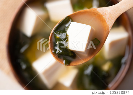 Close up of wooden spoon scooping miso soup with soft tofu and seaweed from a wooden bowl, Top view 135828874