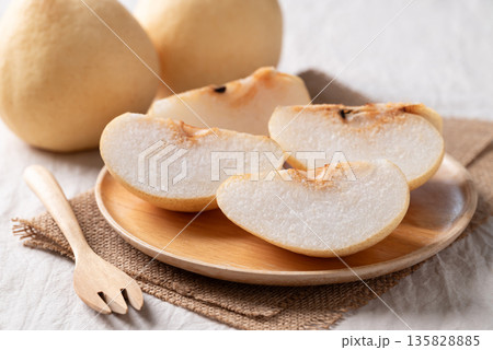 Sliced Asian pears on a wooden plate over burlap fabric with a fork on white fabric background 135828885