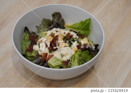 top view Caesar salad bacon, croutons, tomatoes, and green vegetables, mayonnaise topped in a white ceramic bowl on wood floor background, food, health, copy space top view Caesar salad bacon, croutons, tomatoes, and green vegetables, mayonnaise topped in a white ceramic bowl on wood floor background, food, health, copy space 135828919