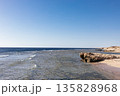 A rocky shoreline overlooking clear waters under a clear blue sky. Textured rock formations, a calm sea surface. The beautiful blue sea of Egypt 135828968
