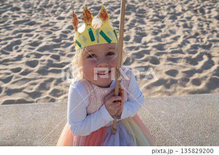 Little girl wearing a paper crown outdoors pretending to be a princess. Little girl wearing a paper crown outdoors pretending to be a princess. 135829200