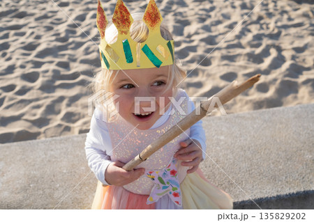 Little girl wearing a paper crown outdoors pretending to be a princess.  135829202