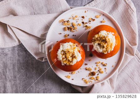 Close up of ripe persimmon filled with cottage cheese, honey and nuts on a plate top view Close up of ripe persimmon filled with cottage cheese, honey and nuts on a plate top view 135829628