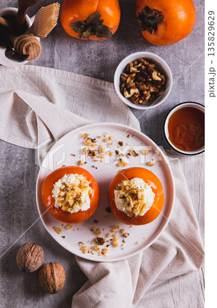 Sweet persimmon stuffed with cottage cheese and walnuts on a plate top and vertical view Sweet persimmon stuffed with cottage cheese and walnuts on a plate top and vertical view 135829629