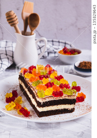 Chocolate cake decorated with gummy bears on a plate on a table vertical view 135829643