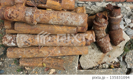 Corroded water pipes removed from the water supply line and lying against the wall of a house, top view, replacement of old rotten sewer pipes, texture of rusting rough iron 135831094