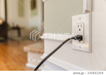 Power cable plugged into American electrical outlet in modern home interior, close view of wall socket and cord with soft blurred background Power cable plugged into American electrical outlet in modern home interior, close view of wall socket and cord with soft blurred background 135831354