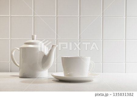 Minimalist kitchen still life with white teapot and cup on light background. Clean modern home and tea time concept. Minimalist kitchen still life with white teapot and cup on light background. Clean modern home and tea time concept. 135831382
