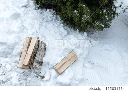 Stack of firewood logs lying on snow near evergreen tree. Winter fuel and rustic outdoor lifestyle concept. 135831384