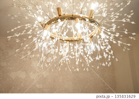Elegant modern chandelier with crystal details and warm glowing light in contemporary interior. Luxury lighting design and home decor concept. Elegant modern chandelier with crystal details and warm glowing light in contemporary interior. Luxury lighting design and home decor concept. 135831629