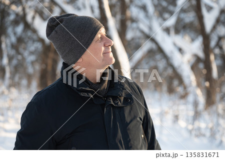 Middle aged man wearing winter hat enjoying sunlight in snowy forest. Peaceful outdoor lifestyle and winter nature concept. Middle aged man wearing winter hat enjoying sunlight in snowy forest. Peaceful outdoor lifestyle and winter nature concept. 135831671