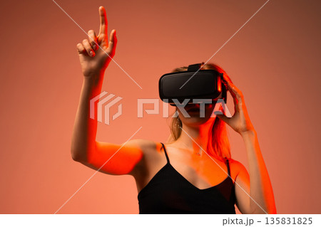 Young woman playing virtual reality game using VR headset and hand gesture control, immersive gaming experience and futuristic entertainment concept Young woman playing virtual reality game using VR headset and hand gesture control, immersive gaming experience and futuristic entertainment concept 135831825