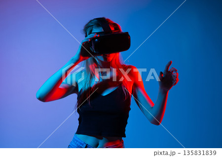 Woman exploring virtual reality environment with VR headset, futuristic metaverse concept with expressive gestures and neon colors 135831839