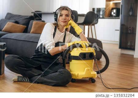 Sitting with vacuum cleaner. Female professional cleaning service worker is domestic room Sitting with vacuum cleaner. Female professional cleaning service worker is domestic room 135832204