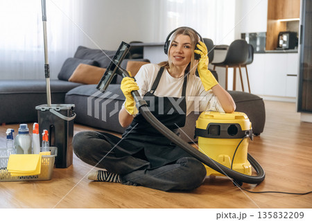 Yellow vacuum cleaner, sitting with it. Female professional cleaning service worker is domestic room Yellow vacuum cleaner, sitting with it. Female professional cleaning service worker is domestic room 135832209