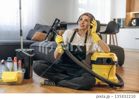 Yellow vacuum cleaner, sitting with it. Female professional cleaning service worker is domestic room Yellow vacuum cleaner, sitting with it. Female professional cleaning service worker is domestic room 135832210