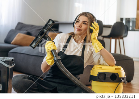 Yellow vacuum cleaner, sitting with it. Female professional cleaning service worker is domestic room Yellow vacuum cleaner, sitting with it. Female professional cleaning service worker is domestic room 135832211