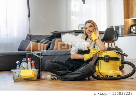 Resting, sitting on the floor. Female professional cleaning service worker is domestic room 135832228