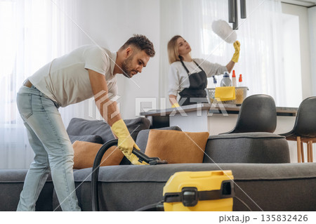 Modern yellow vacuum cleaner, busy. Two cleaning service workers are in domestic room Modern yellow vacuum cleaner, busy. Two cleaning service workers are in domestic room 135832426