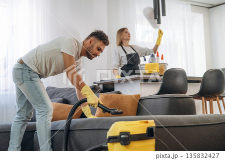 Modern yellow vacuum cleaner, busy. Two cleaning service workers are in domestic room 135832427