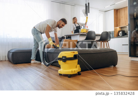 Modern yellow vacuum cleaner, busy. Two cleaning service workers are in domestic room 135832428